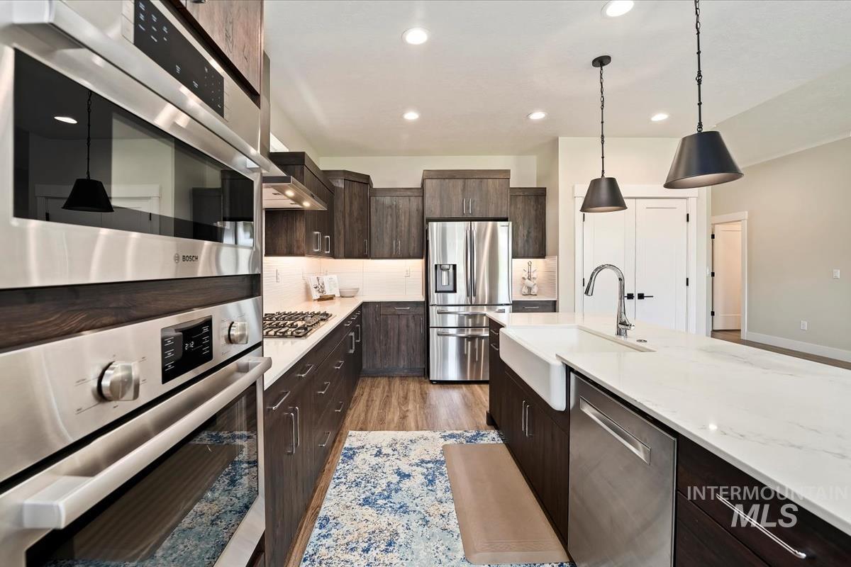 Kitchen with dark brown cabinetry, stainless steel appliances, light wood-style floors, modern cabinets, and tasteful backsplash