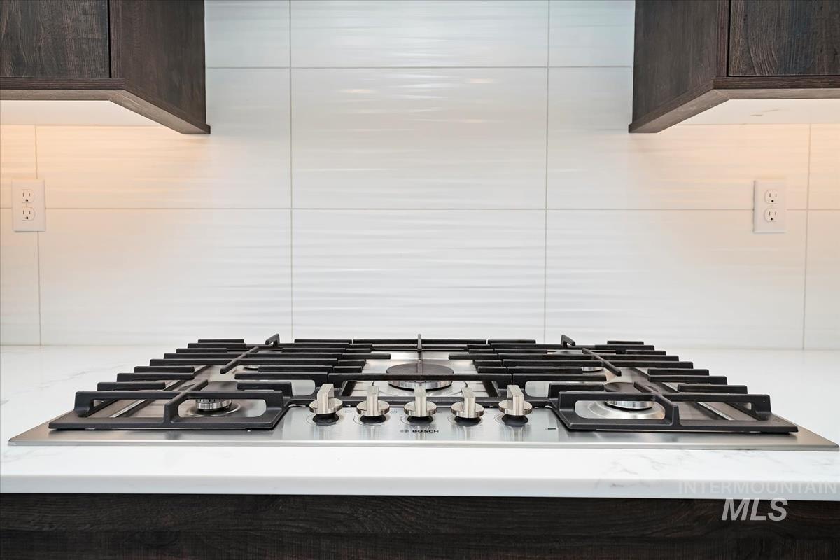 Kitchen view of dark brown cabinetry, stainless steel gas stovetop, and light stone countertops