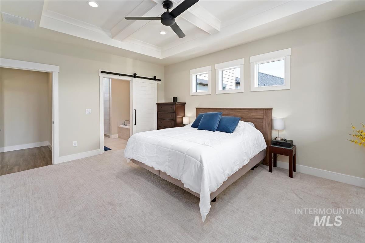 Bedroom with a barn door, beamed ceiling, carpet flooring, ensuite bathroom, and coffered ceiling