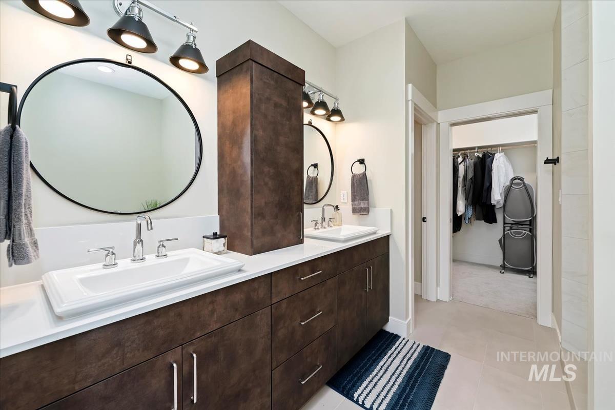 Bathroom with a walk in closet, double vanity, and light tile patterned floors