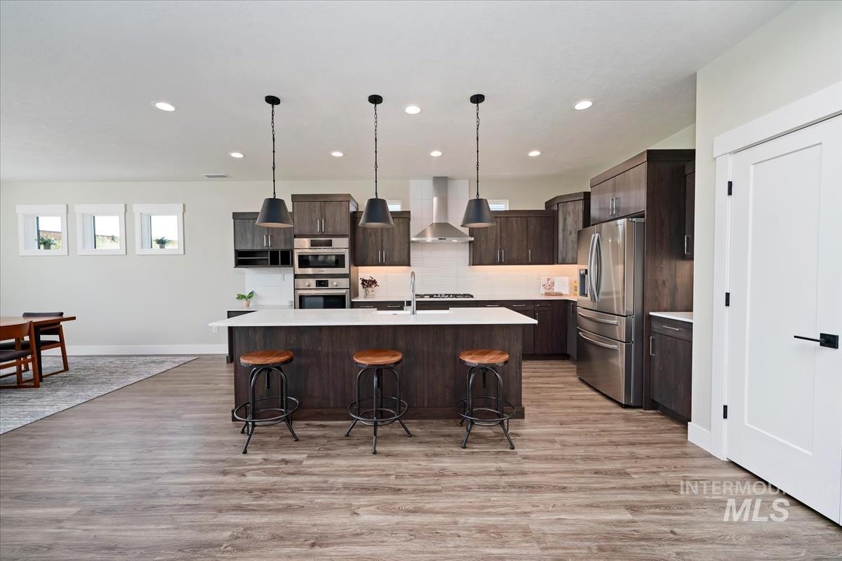 Kitchen featuring decorative light fixtures, stainless steel appliances, wall chimney range hood, dark brown cabinets, and recessed lighting