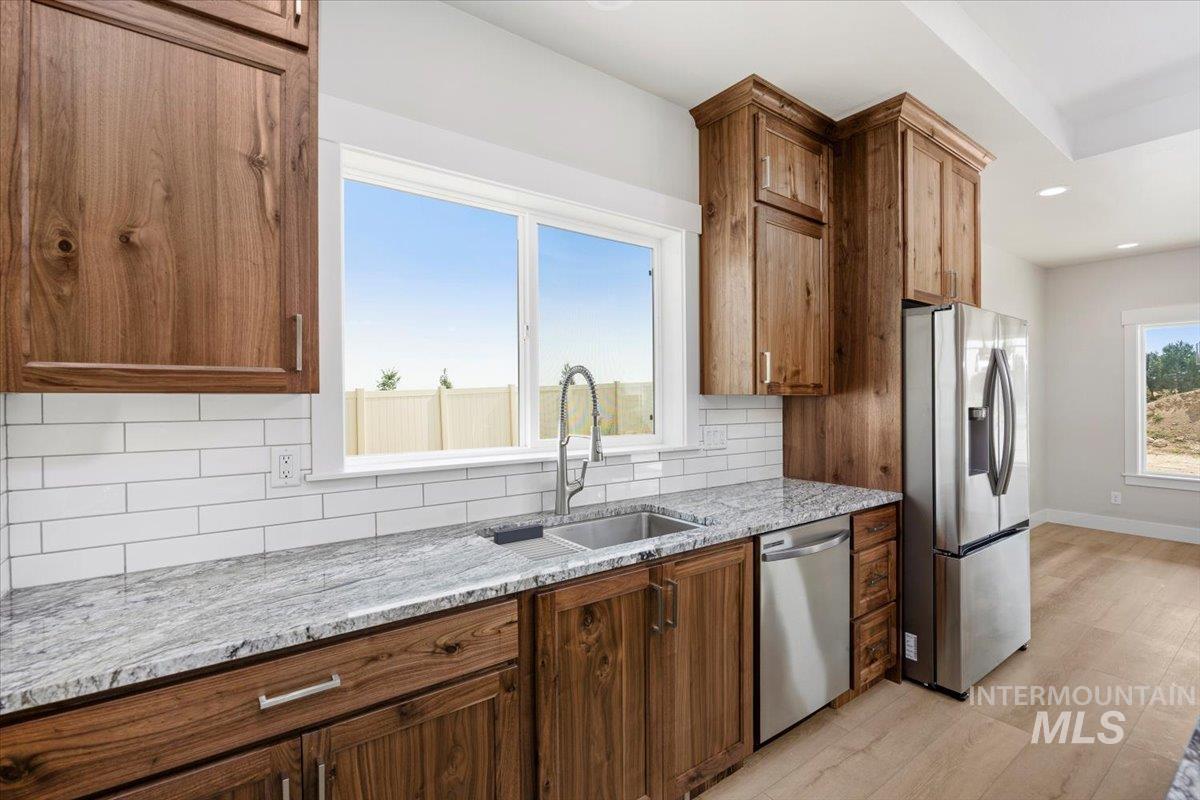 Kitchen featuring tasteful backsplash, light stone countertops, appliances with stainless steel finishes, brown cabinetry, and recessed lighting