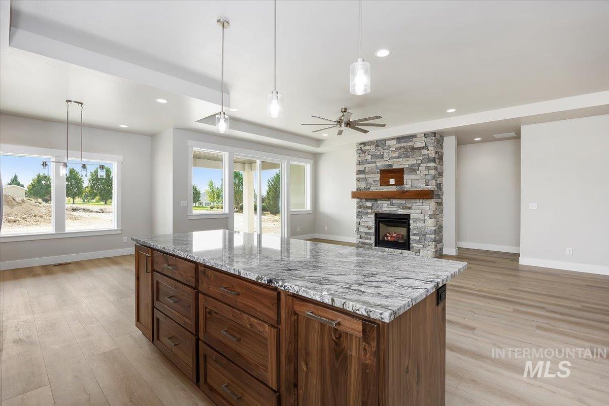 Kitchen featuring hanging light fixtures, light stone countertops, a ceiling fan, a stone fireplace, and a tray ceiling