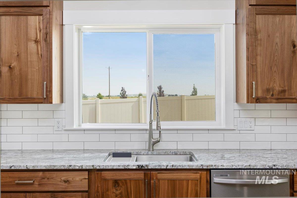 Kitchen with brown cabinets, backsplash, light stone counters, and dishwasher