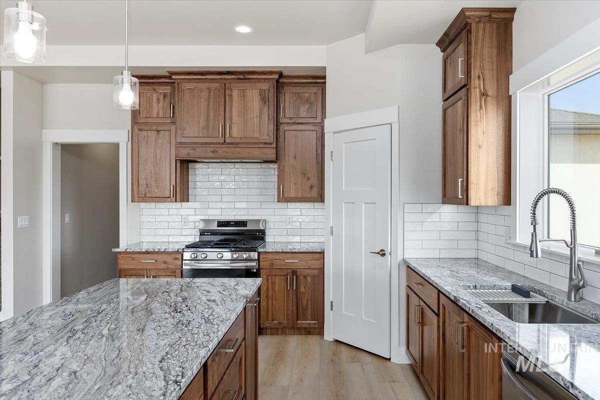 Kitchen featuring light stone counters, appliances with stainless steel finishes, tasteful backsplash, decorative light fixtures, and brown cabinetry