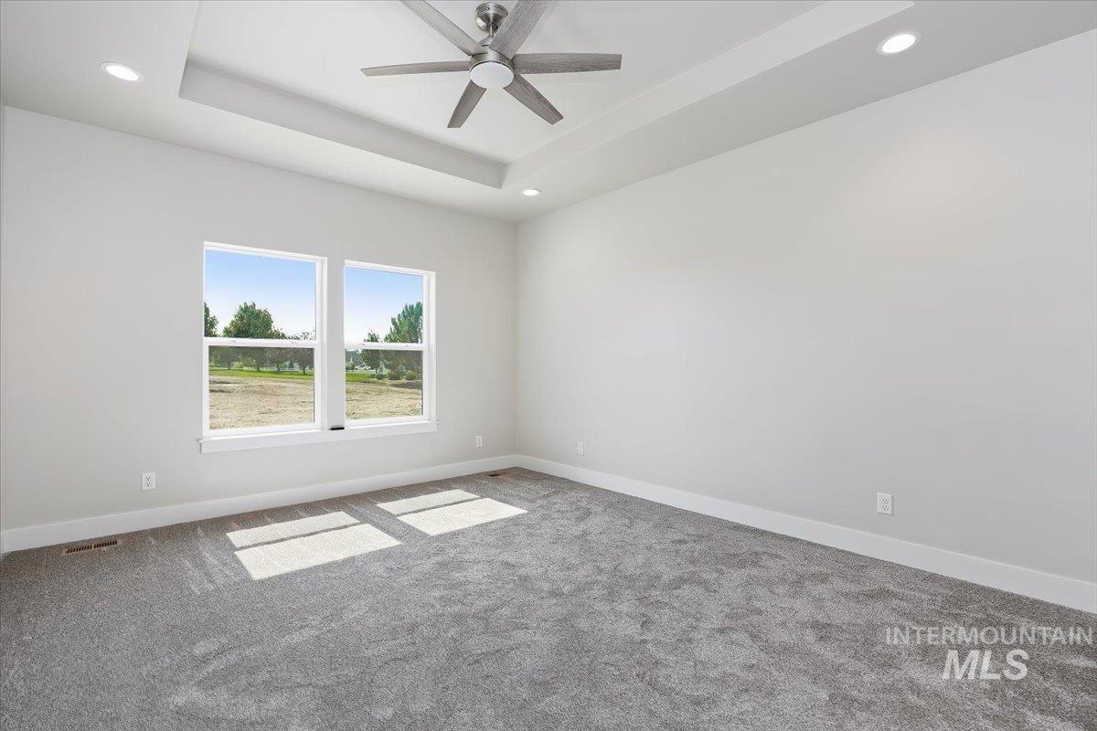 Empty room featuring a tray ceiling, carpet floors, recessed lighting, and a ceiling fan