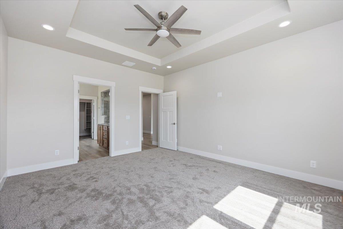Unfurnished bedroom featuring a tray ceiling, light colored carpet, recessed lighting, connected bathroom, and a ceiling fan