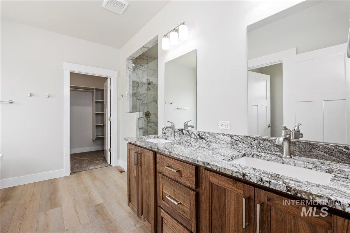 Bathroom with a marble finish shower, double vanity, light wood-style floors, and a walk in closet