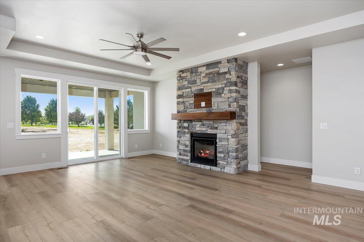 Unfurnished living room with a tray ceiling, a stone fireplace, light wood finished floors, ceiling fan, and recessed lighting