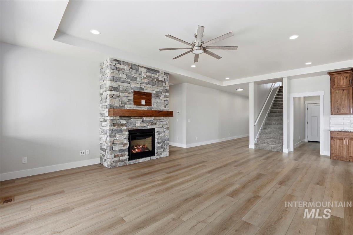 Unfurnished living room with light wood finished floors, ceiling fan, a stone fireplace, recessed lighting, and stairs