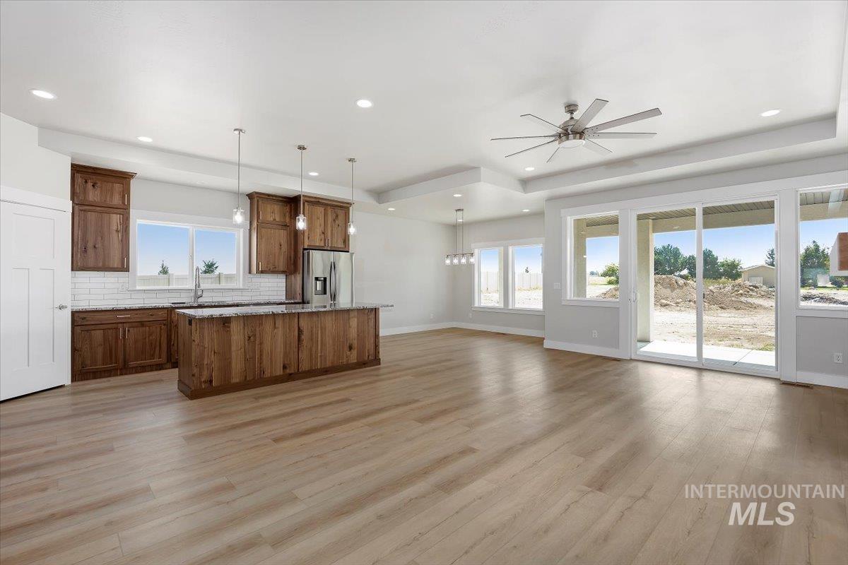 Kitchen with a raised ceiling, open floor plan, pendant lighting, a kitchen island, and tasteful backsplash