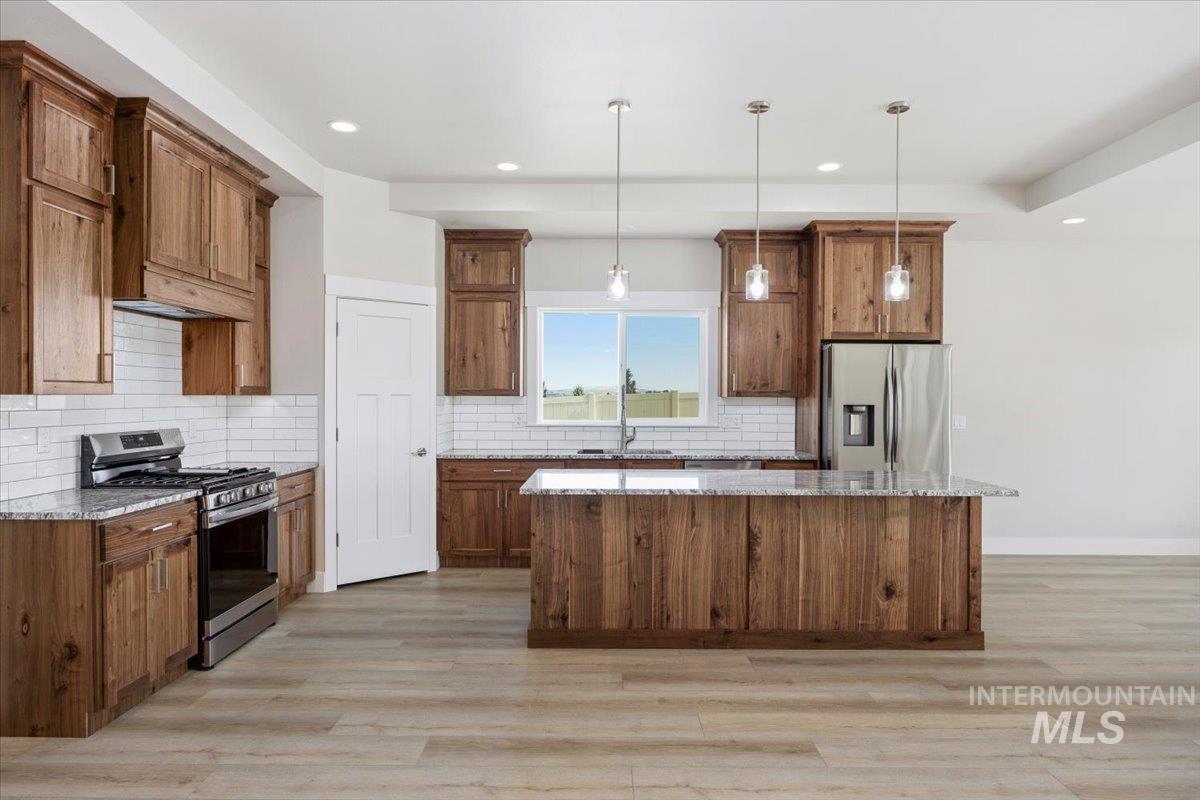 Kitchen featuring stainless steel appliances, hanging light fixtures, light stone counters, tasteful backsplash, and a kitchen island