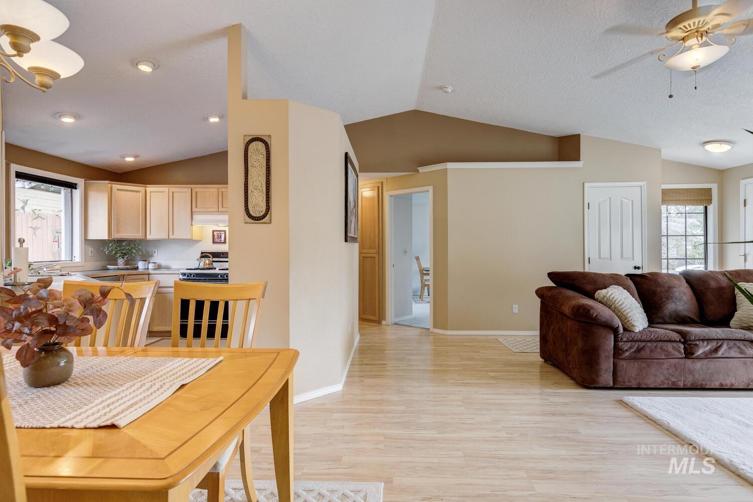 Living area featuring lofted ceiling, healthy amount of natural light, light wood finished floors, and a ceiling fan