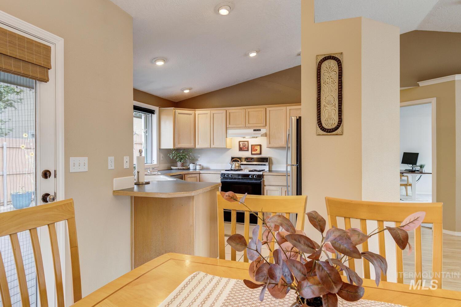 Kitchen with lofted ceiling, light countertops, gas range, freestanding refrigerator, and light brown cabinets