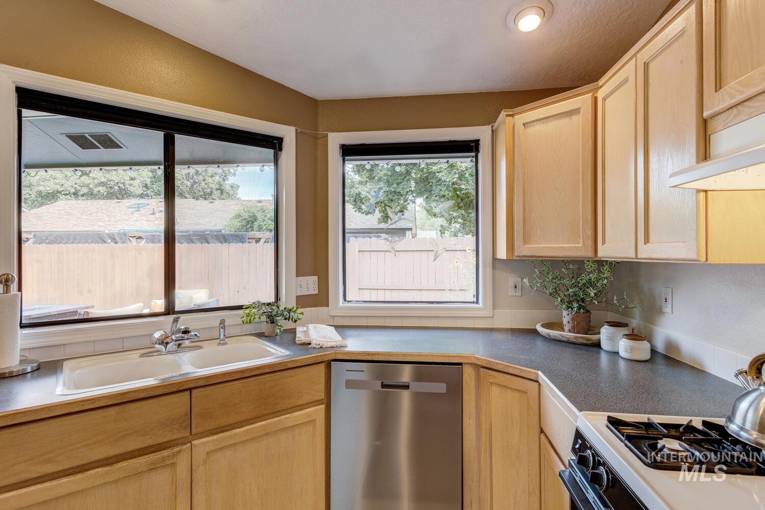 Kitchen featuring light brown cabinetry, dishwasher, black gas range, and dark countertops