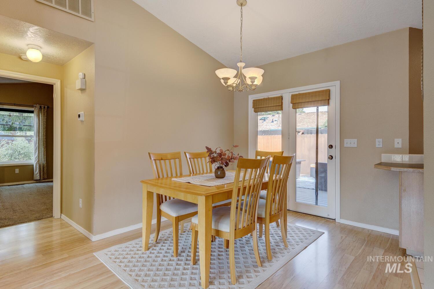 Dining area featuring light wood-style flooring, vaulted ceiling, and a chandelier