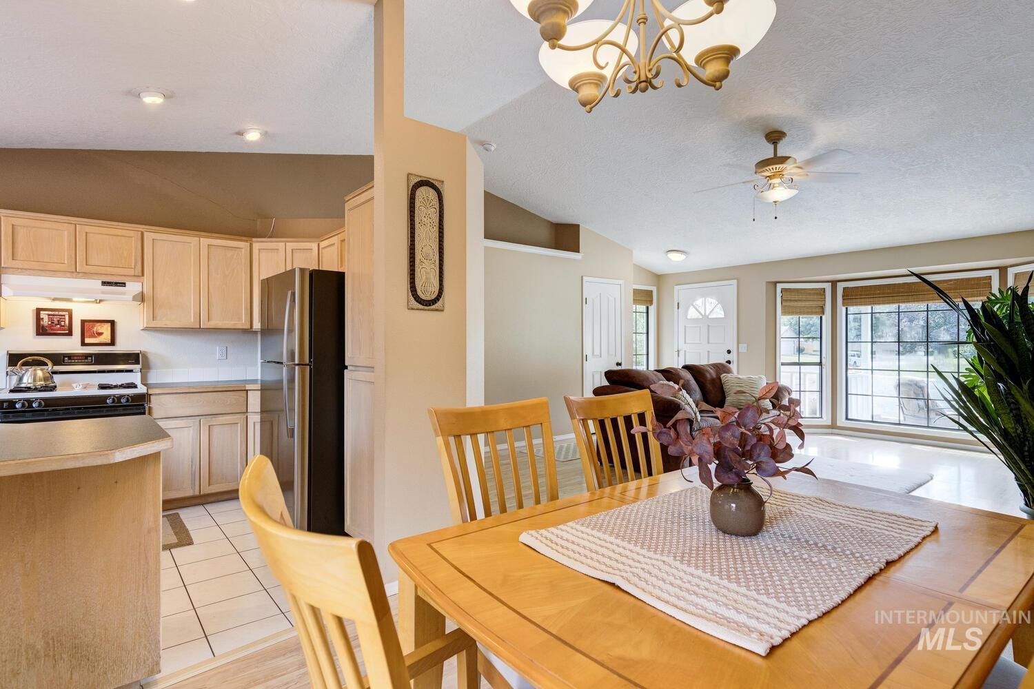Dining space with vaulted ceiling, light tile patterned floors, a chandelier, a ceiling fan, and a textured ceiling