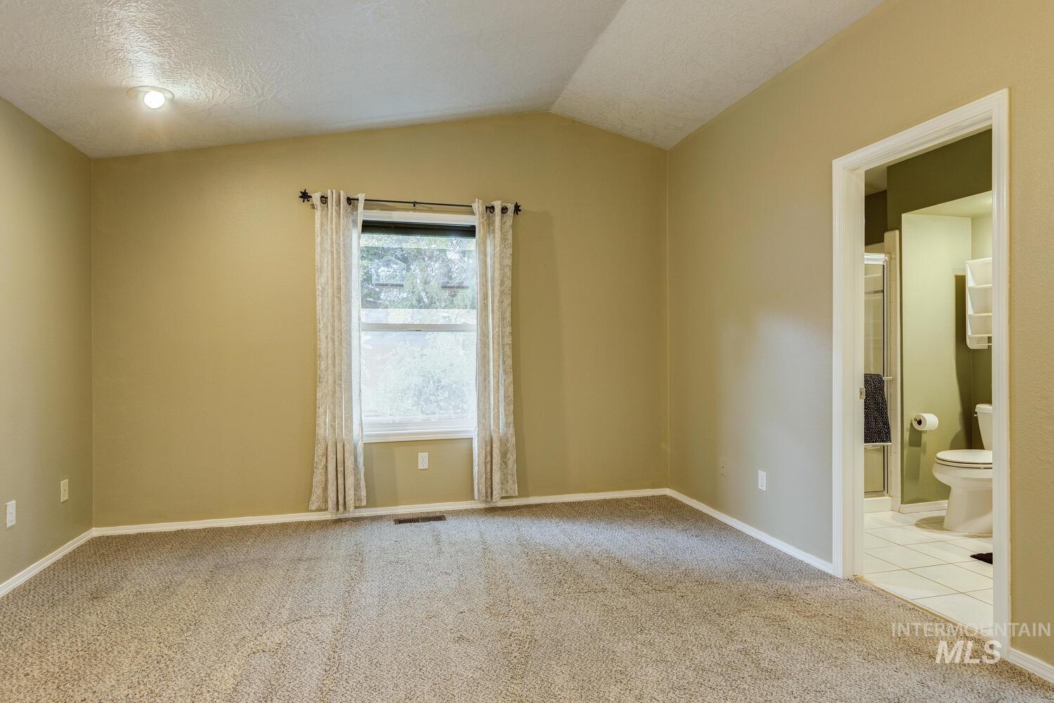 Empty room featuring light carpet, a textured ceiling, and vaulted ceiling