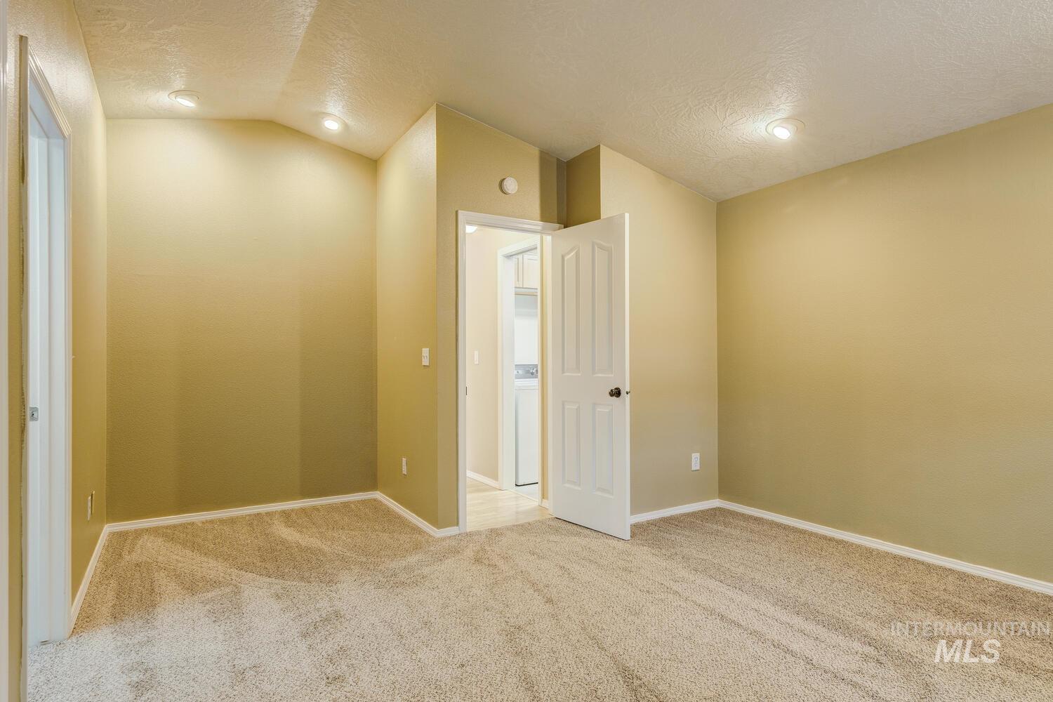 Carpeted empty room with a textured ceiling, lofted ceiling, washer / clothes dryer, and recessed lighting