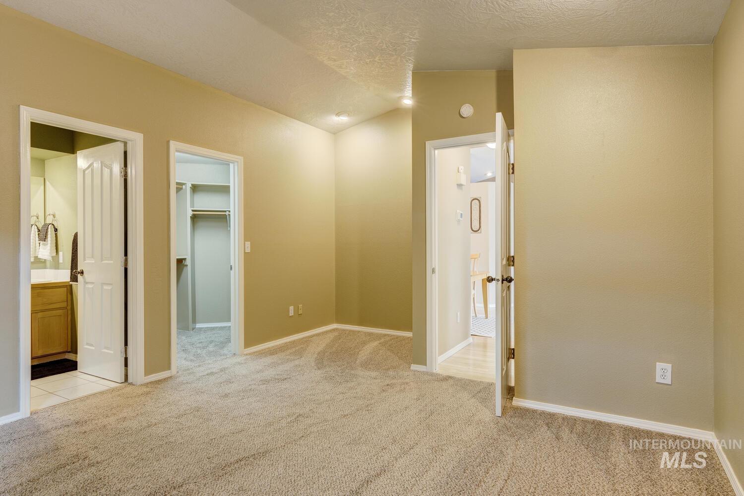 Corridor with lofted ceiling, light colored carpet, and a textured ceiling