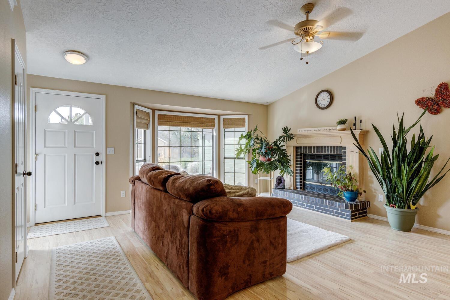 Living area with a textured ceiling, light wood finished floors, vaulted ceiling, a fireplace, and ceiling fan