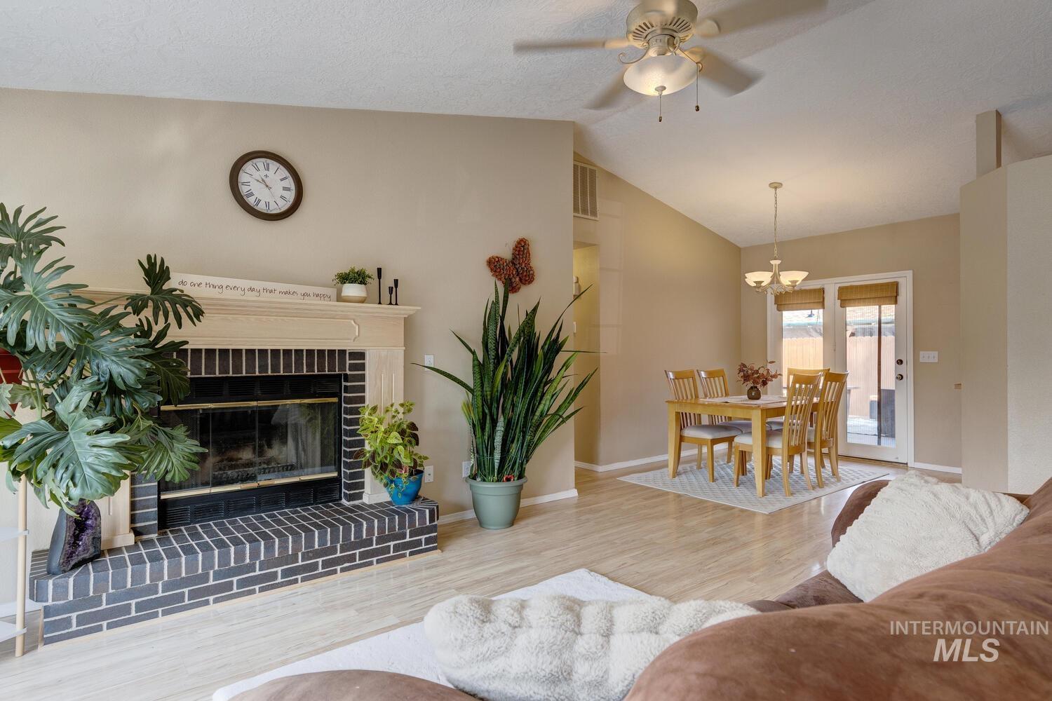 Living room with wood finished floors, lofted ceiling, a brick fireplace, ceiling fan, and a chandelier