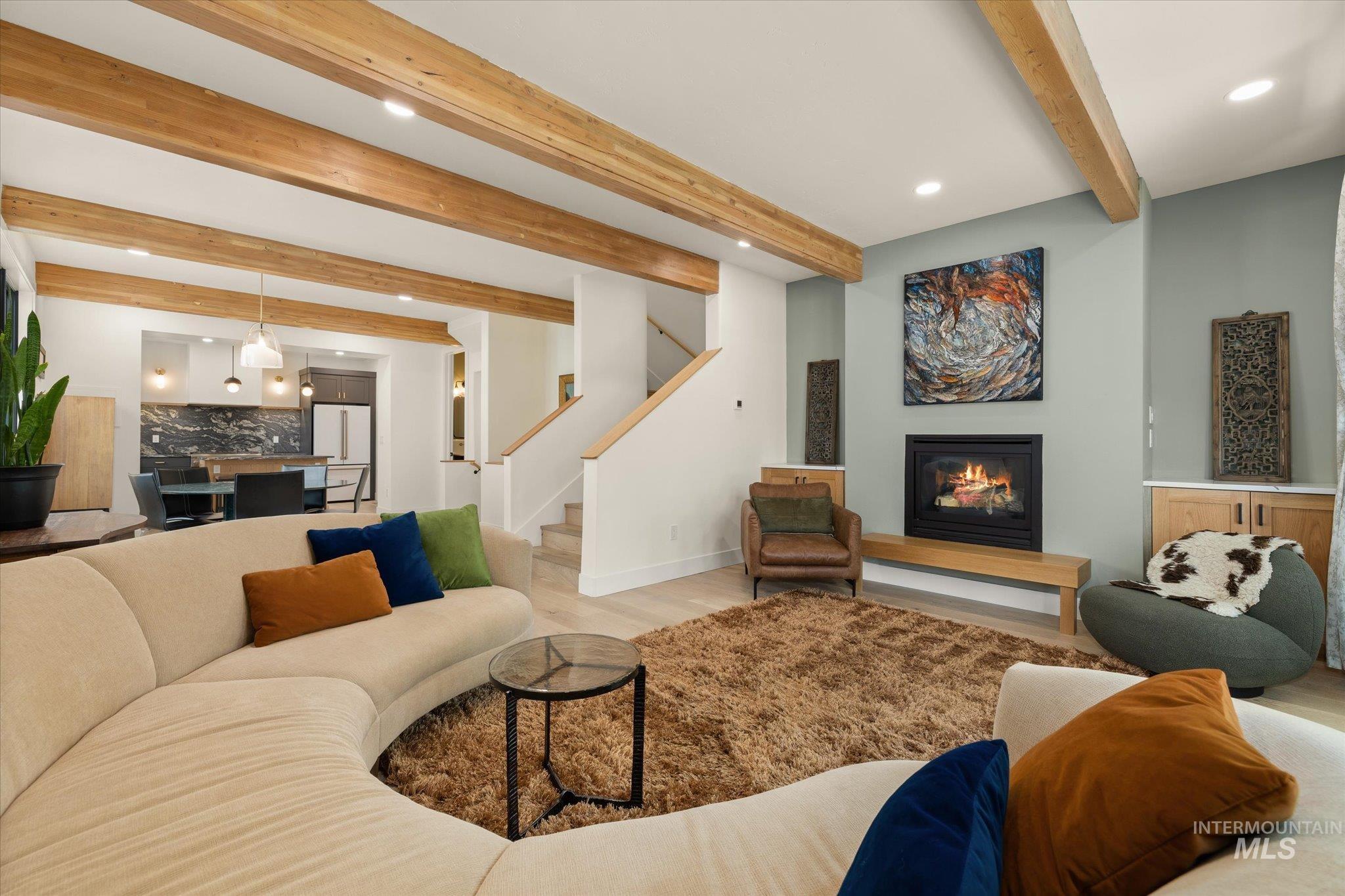 Living area with beam ceiling, recessed lighting, wood finished floors, a glass covered fireplace, and stairs