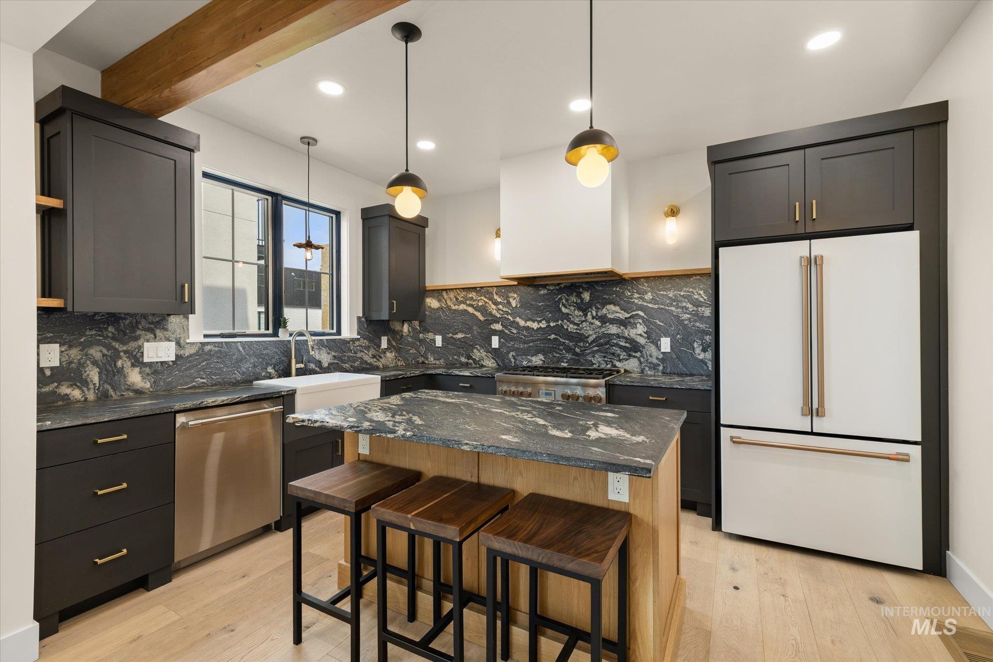 Kitchen featuring dark stone counters, appliances with stainless steel finishes, decorative light fixtures, light wood finished floors, and recessed lighting
