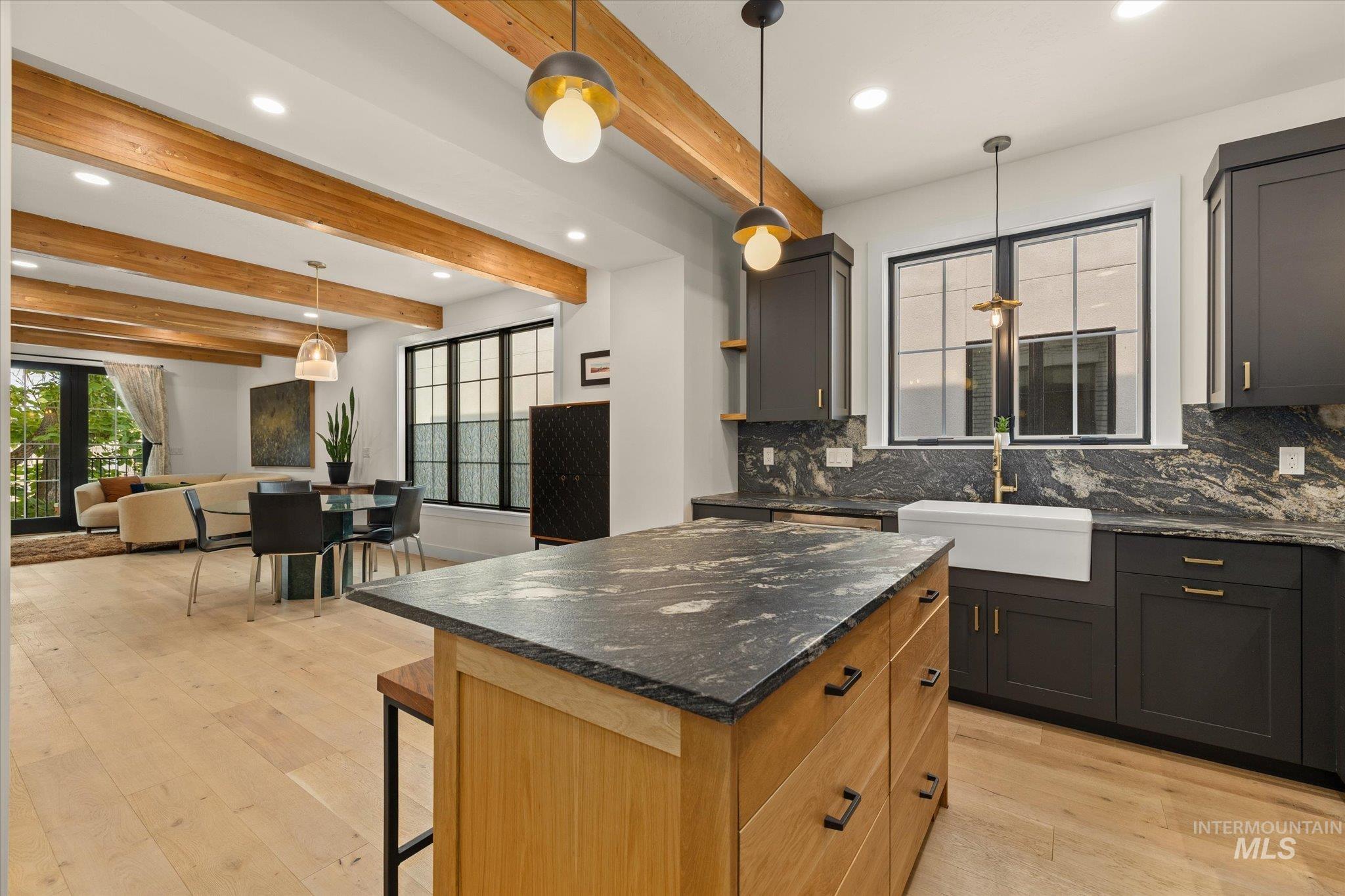 Kitchen with hanging light fixtures, decorative backsplash, beam ceiling, dark stone counters, and light wood-style flooring