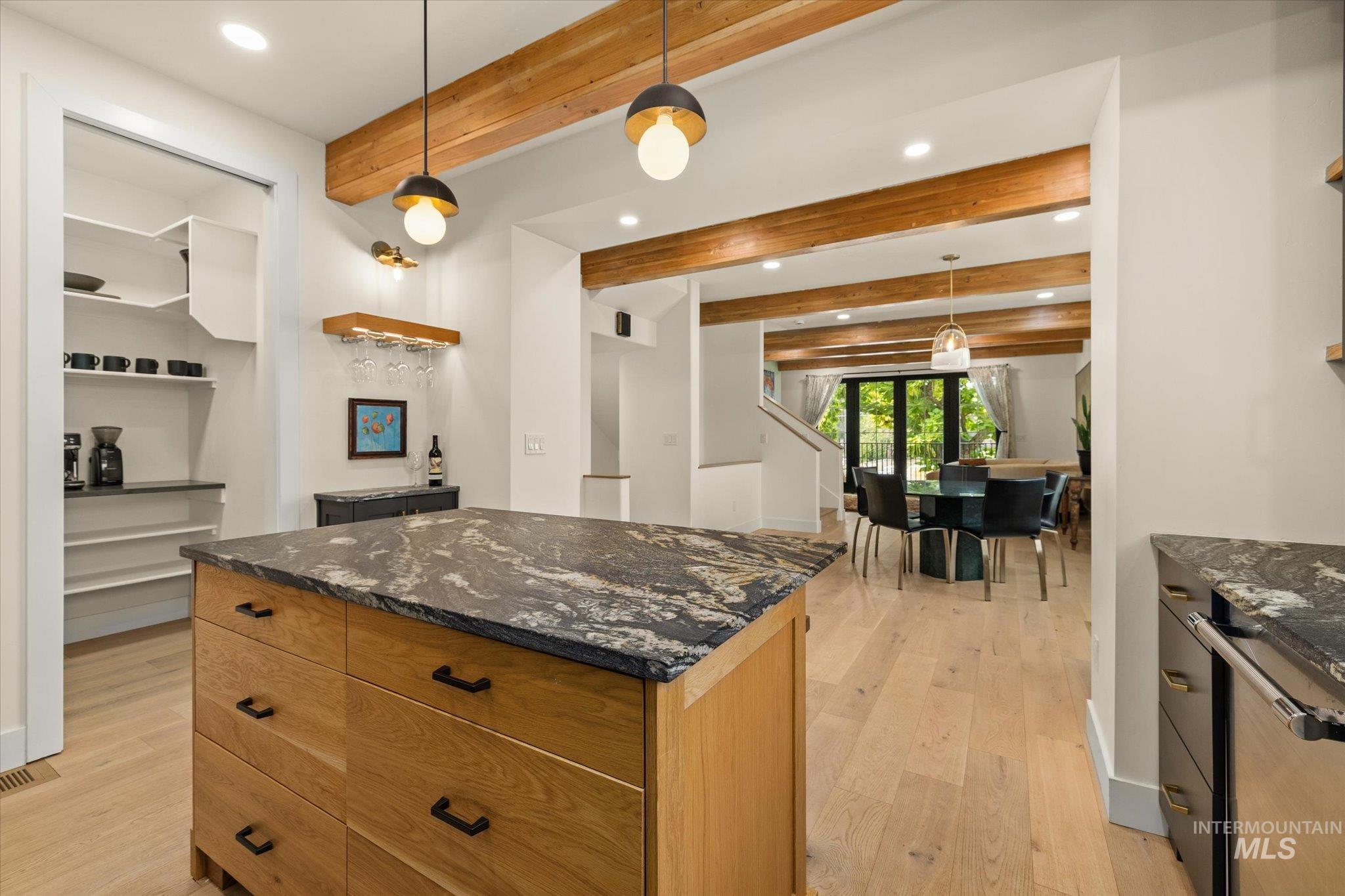 Kitchen with beam ceiling, dark stone countertops, light wood-style floors, recessed lighting, and hanging light fixtures