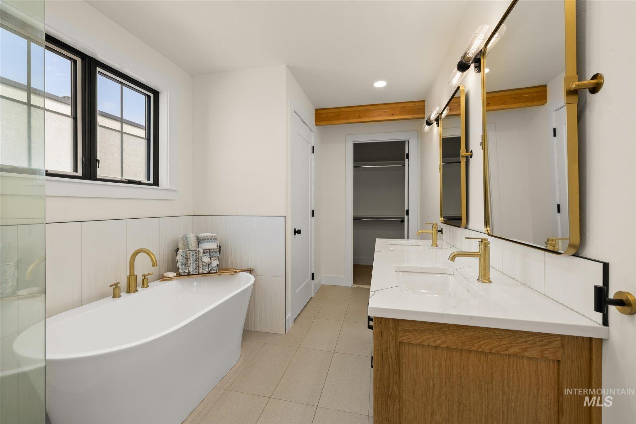 Full bath featuring a soaking tub, double vanity, light tile patterned flooring, a spacious closet, and a wainscoted wall