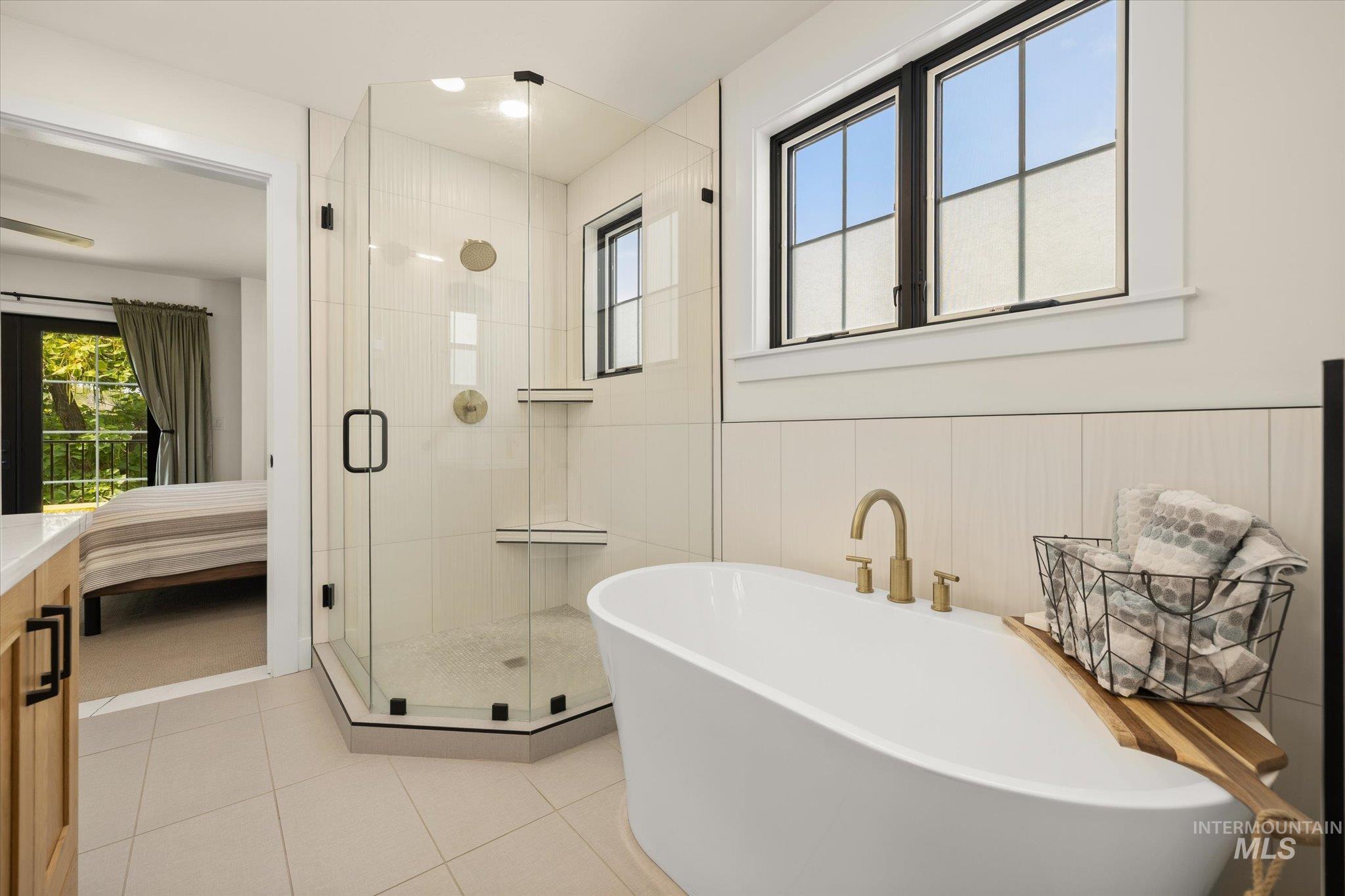 Bathroom with connected bathroom, plenty of natural light, a freestanding tub, a shower stall, and a wainscoted wall