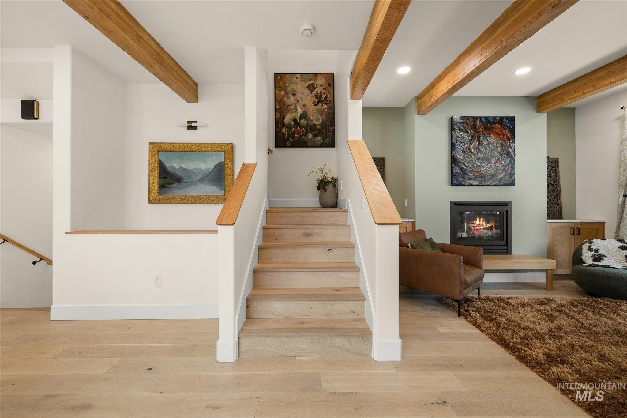 Stairway featuring beamed ceiling, a glass covered fireplace, wood finished floors, and recessed lighting