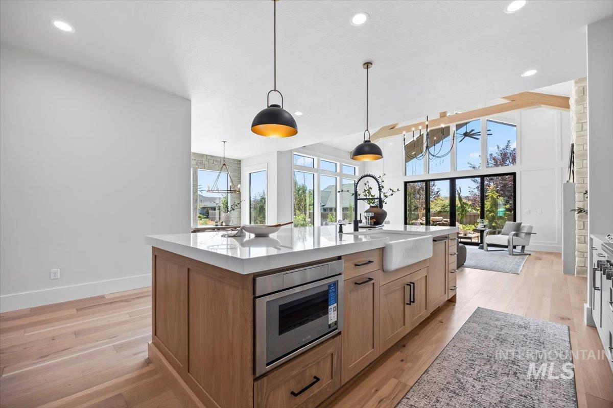Kitchen with light wood-type flooring, an island with sink, hanging light fixtures, recessed lighting, and light stone counters