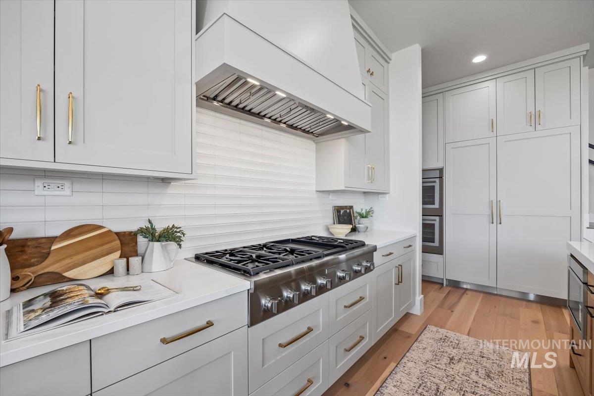 Kitchen featuring custom range hood, stainless steel appliances, light countertops, light wood-type flooring, and recessed lighting