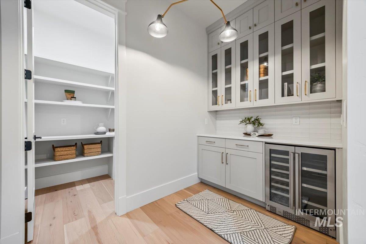 Bar featuring wine cooler, light wood-type flooring, and tasteful backsplash
