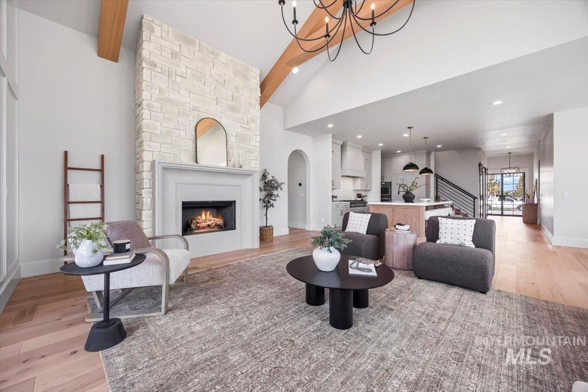 Living room featuring beamed ceiling, a chandelier, light wood-style flooring, a large fireplace, and stairway