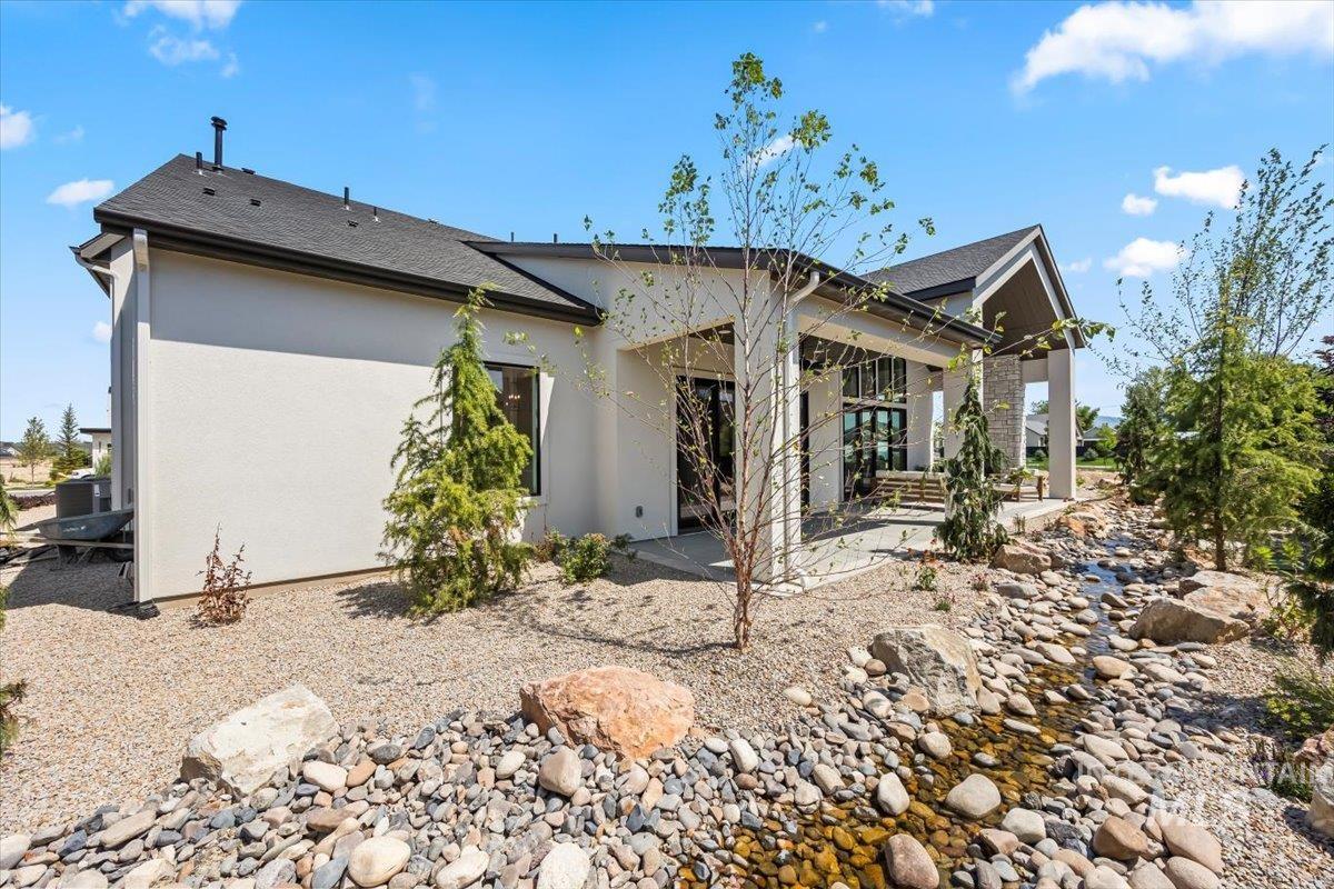 Back of house with a shingled roof, a patio area, and stucco siding