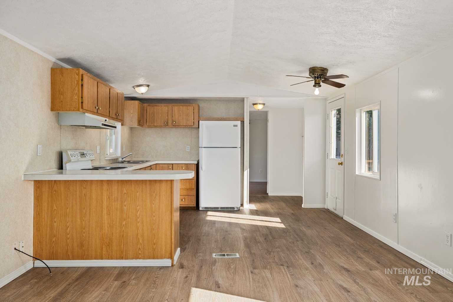 Kitchen with light countertops, white appliances, dark wood-style flooring, brown cabinets, and a peninsula