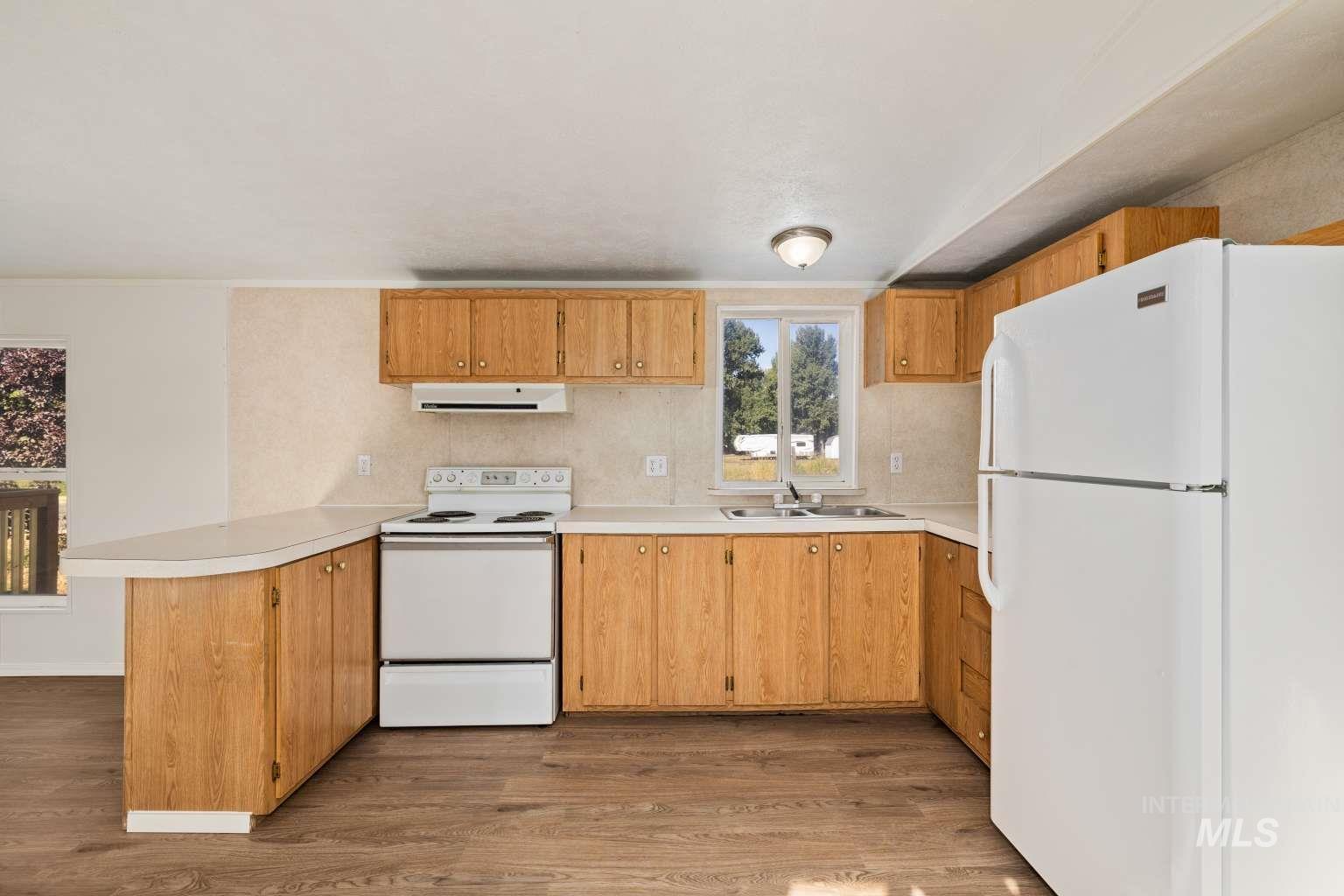 Kitchen with white appliances, light countertops, light wood-type flooring, under cabinet range hood, and a peninsula