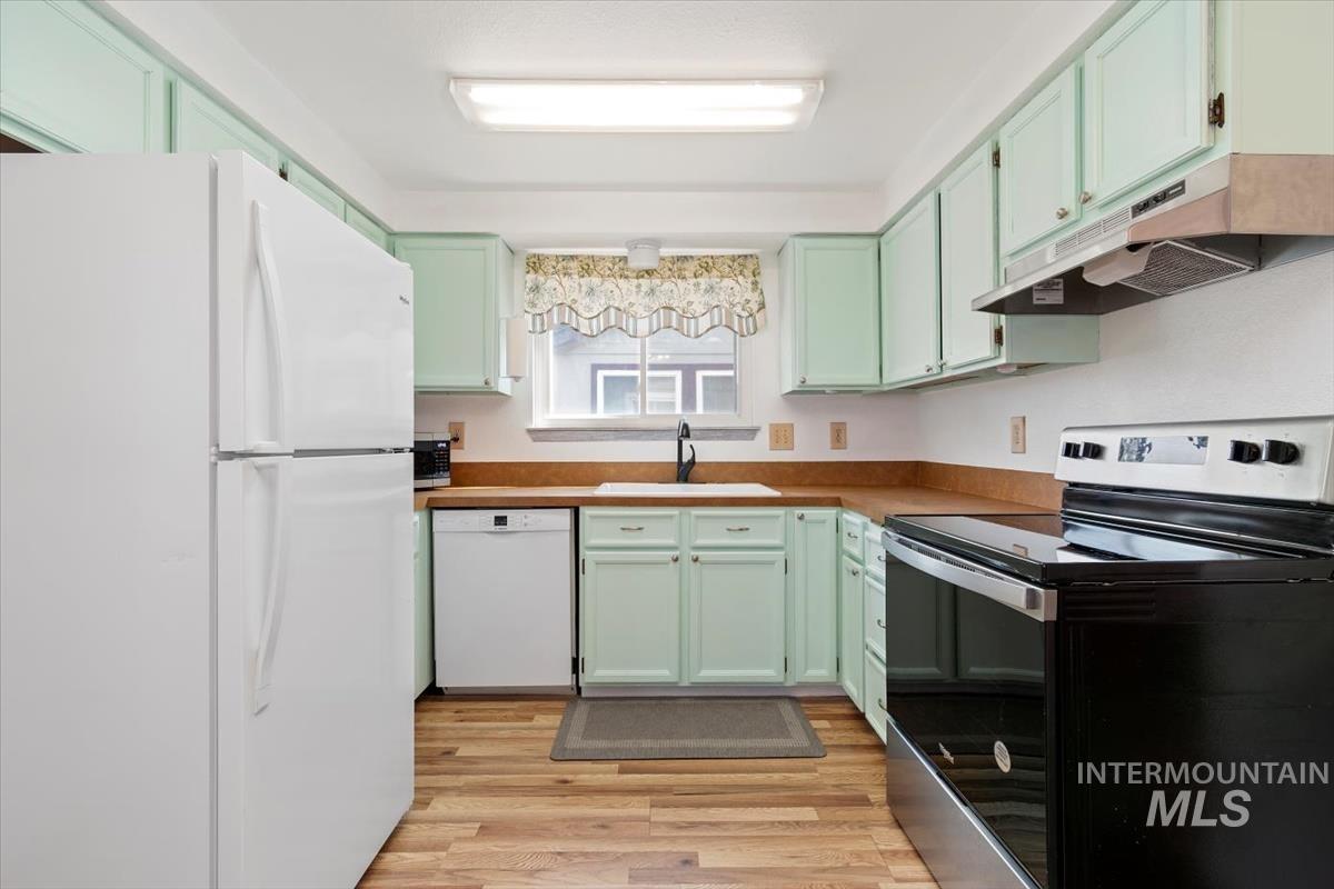 Kitchen with white appliances, under cabinet range hood, light wood finished floors, and green cabinets