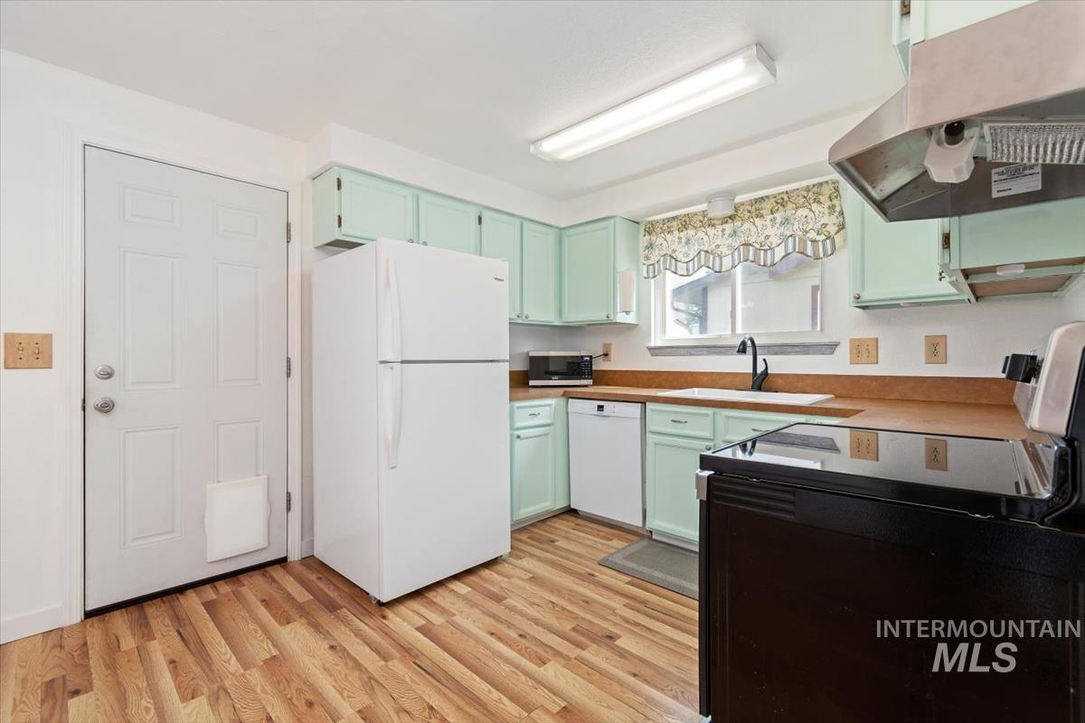 Kitchen featuring white appliances, island exhaust hood, light wood-style floors, and light countertops