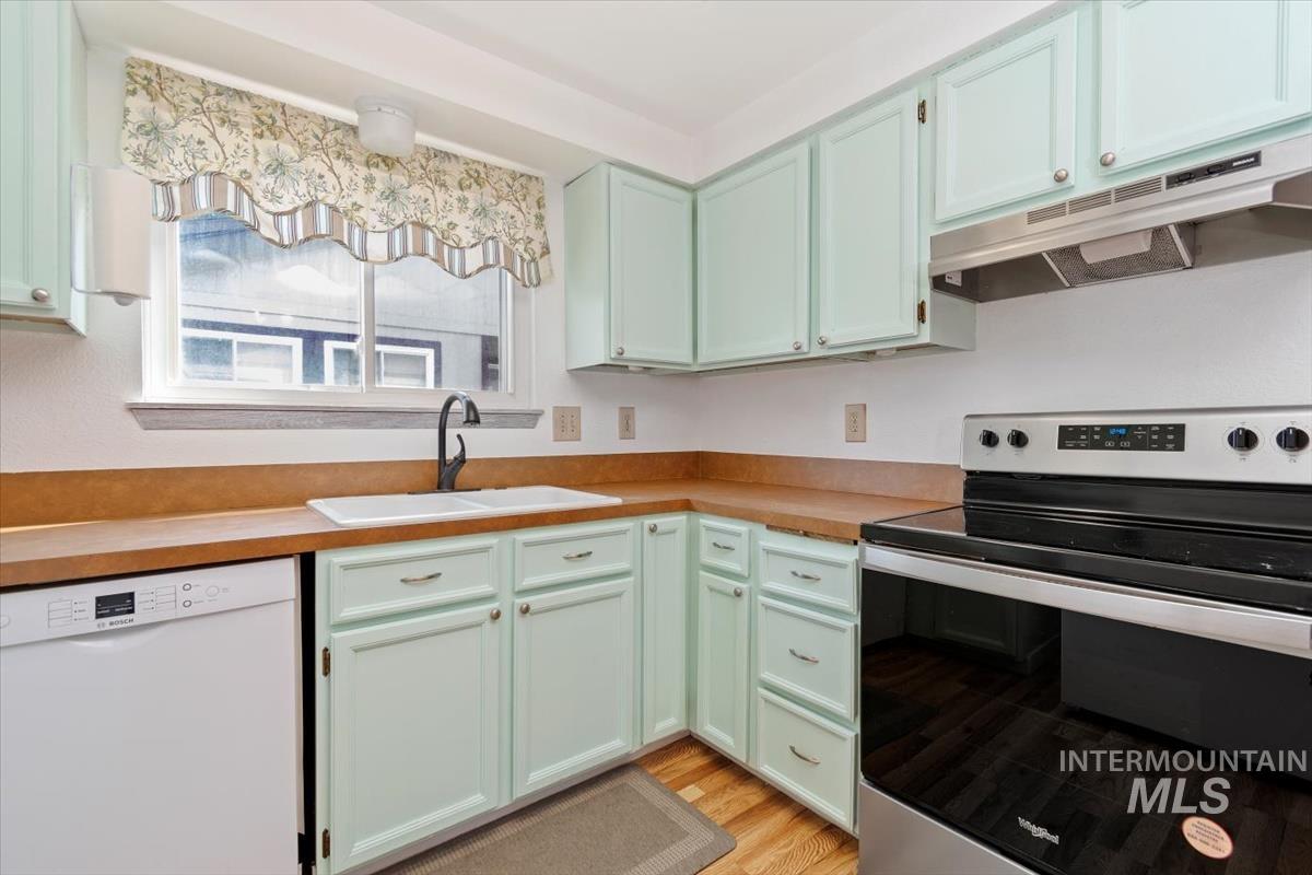 Kitchen featuring stainless steel electric range oven, dishwasher, light countertops, under cabinet range hood, and light wood finished floors