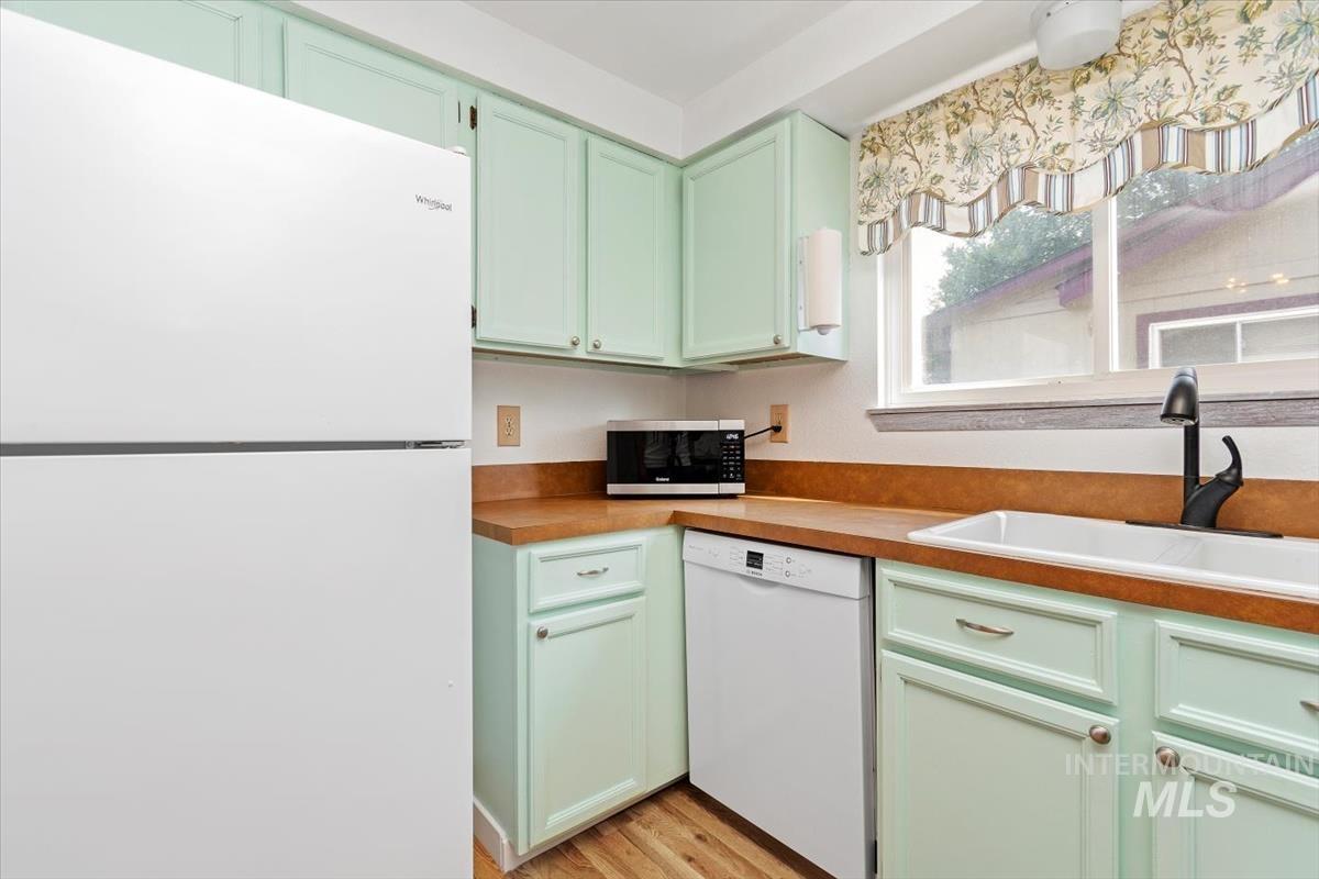 Kitchen featuring green cabinetry, white appliances, light wood finished floors, and light countertops