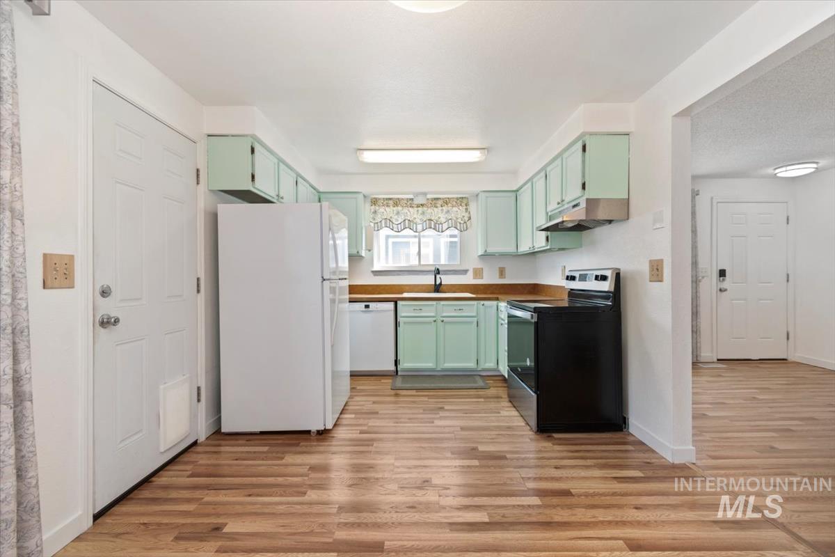 Kitchen with white appliances, green cabinetry, light wood-type flooring, and under cabinet range hood