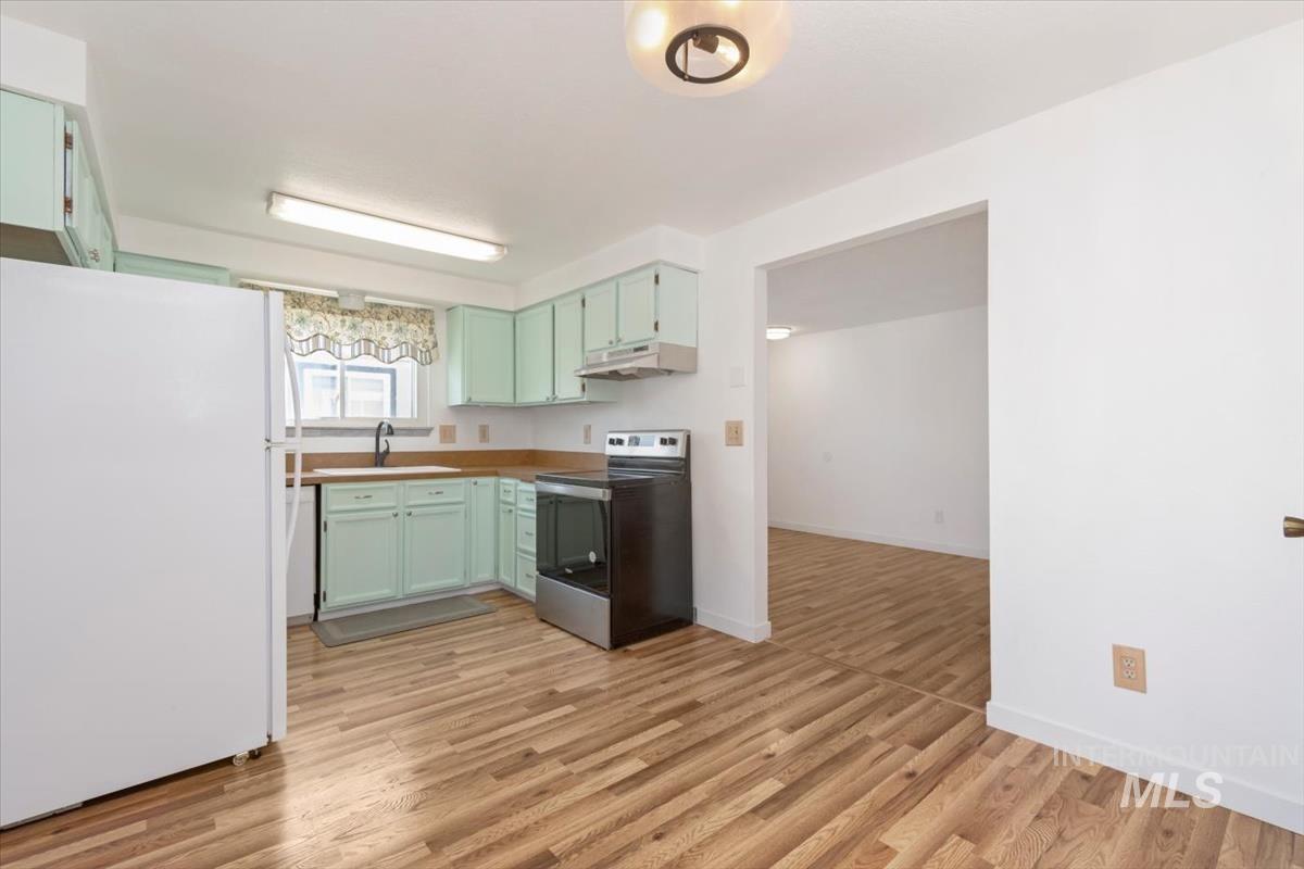 Kitchen featuring freestanding refrigerator, stainless steel range with electric cooktop, light wood-style flooring, and green cabinetry