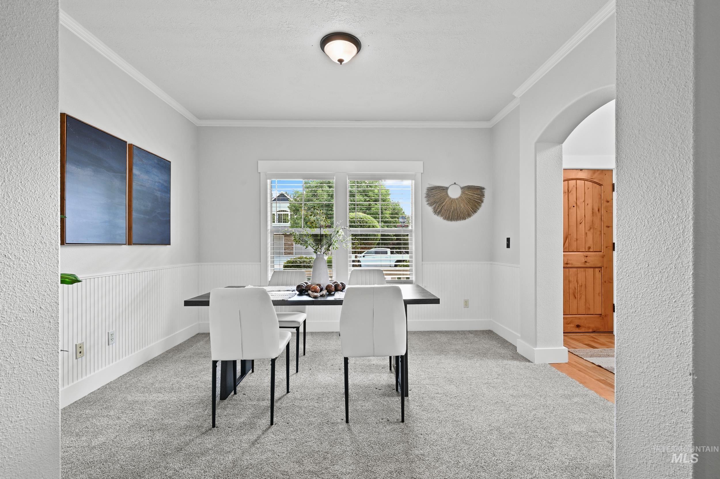 Dining area with arched walkways, ornamental molding, and light carpet