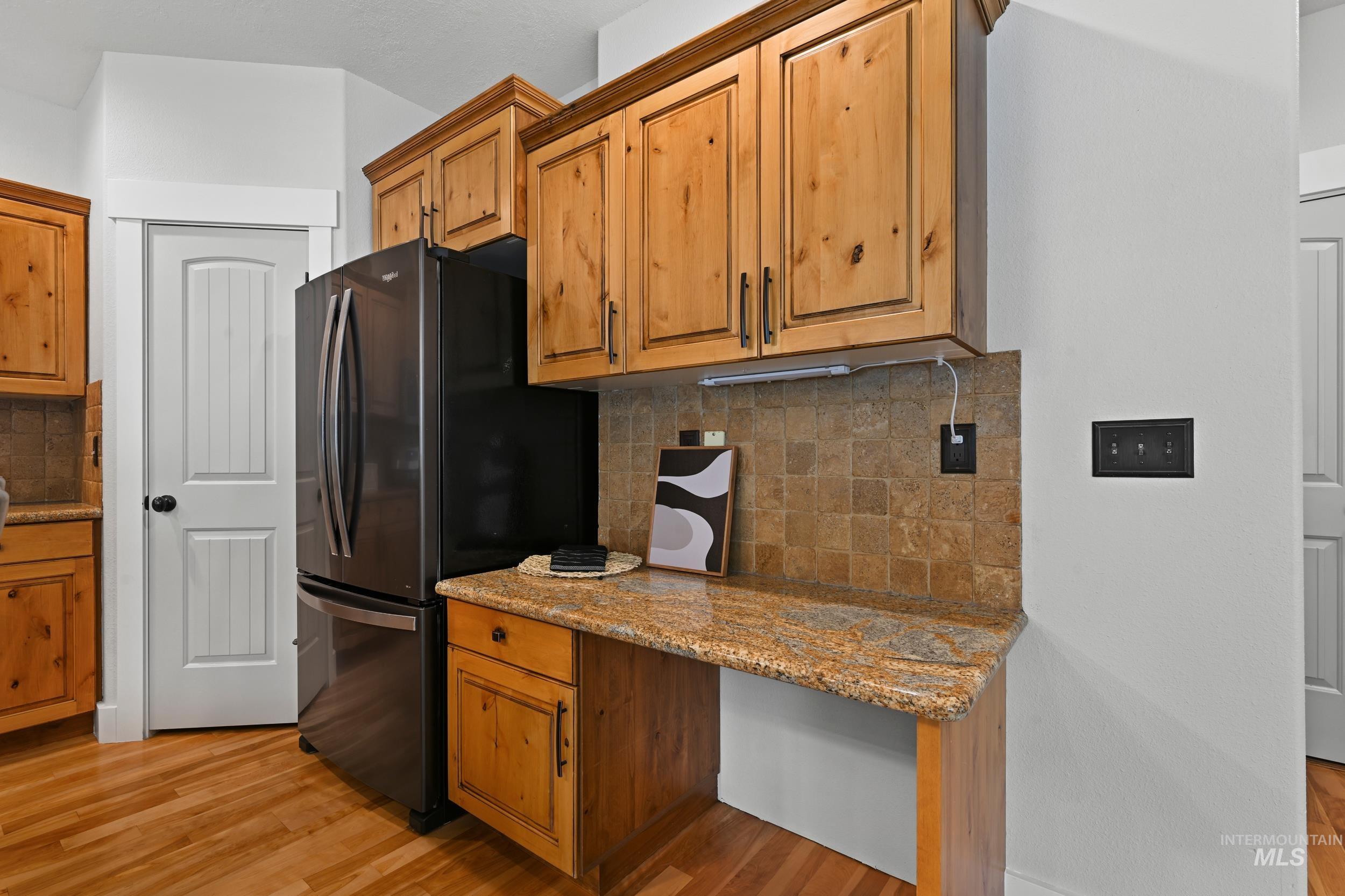Kitchen featuring backsplash, light stone countertops, freestanding refrigerator, and light wood-type flooring