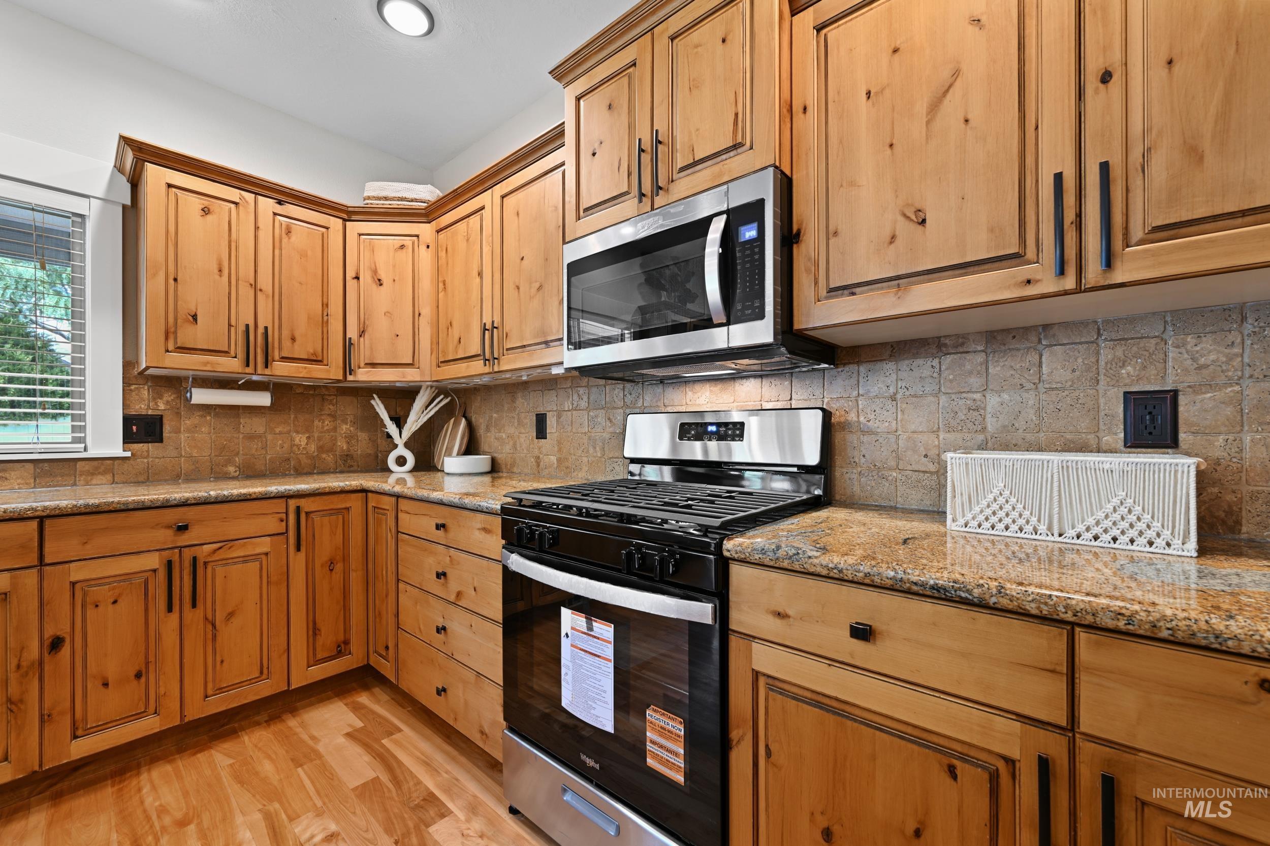 Kitchen with appliances with stainless steel finishes, light wood-style flooring, light stone counters, decorative backsplash, and recessed lighting