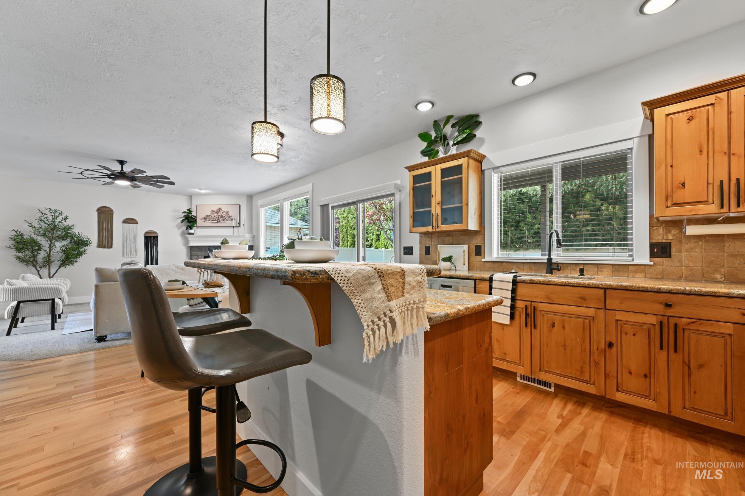 Kitchen featuring a breakfast bar, decorative light fixtures, light stone counters, brown cabinetry, and a textured ceiling